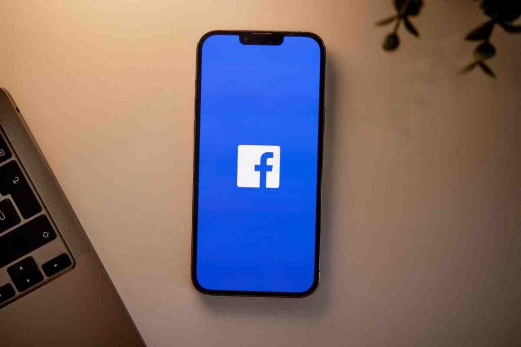 Smartphone showing the Facebook logo beside a laptop, related to a Facebook Pixel Shopify setup issue