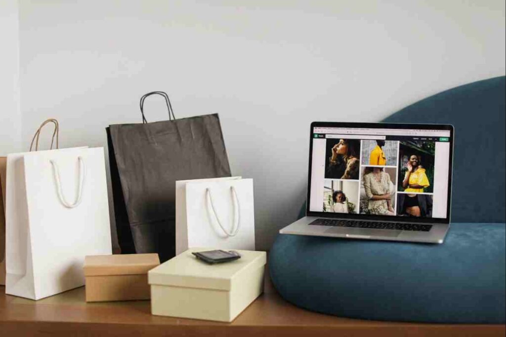 Shopify vs Etsy: laptop showing fashion photos beside paper shopping bags and gift boxes on a blue sofa