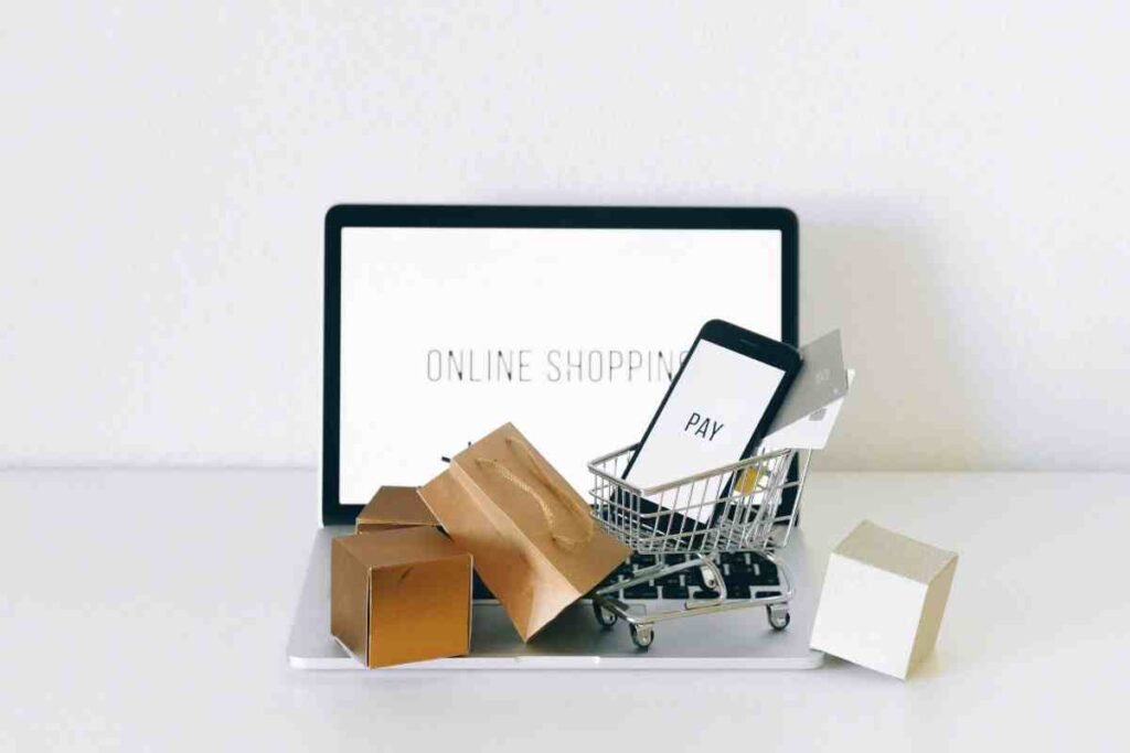 Shopify vs Etsy: laptop showing online shopping with mini cart, smartphone pay screen, credit card and paper bags