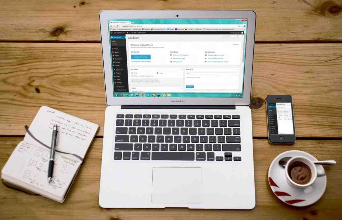 WordPress dashboard open on a laptop beside a phone, notebook and coffee, illustrating a WordPress SEO setup guide